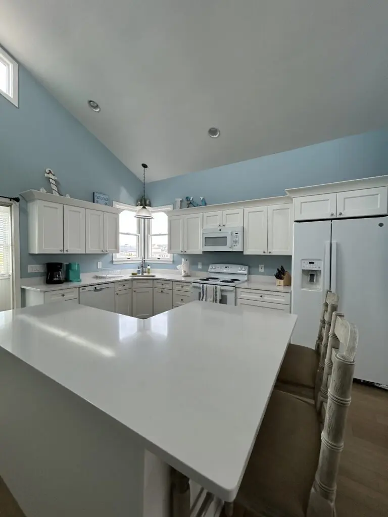 Clean, bright kitchen with white cabinets, polished countertops, white appliances, blue walls, vaulted ceiling, and a spacious island after professional cleaning.