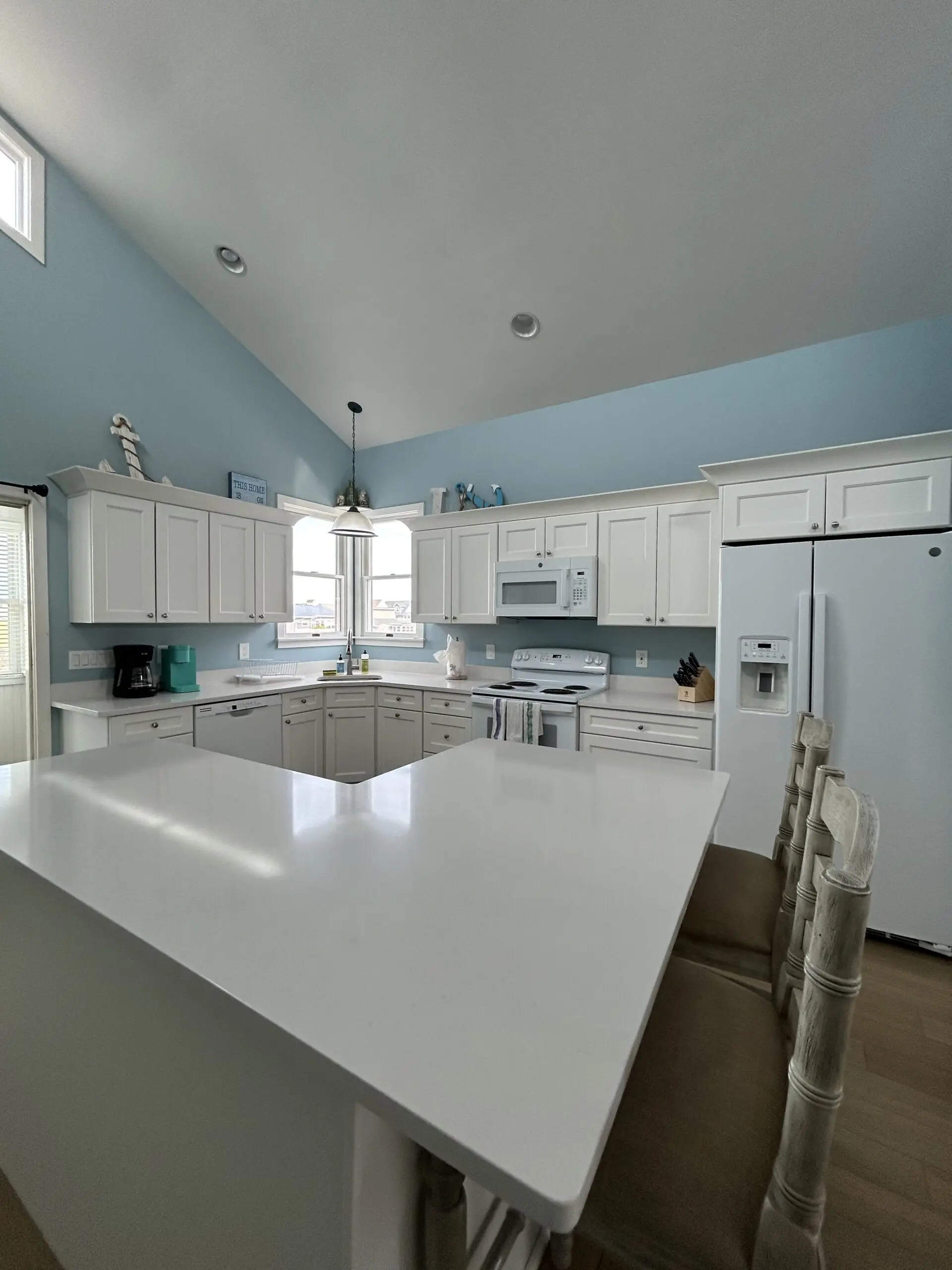 Clean, bright kitchen with white cabinets, polished countertops, white appliances, blue walls, vaulted ceiling, and a spacious island after professional cleaning.