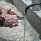 Close-up of hands being washed with soap under running water from an outdoor tap