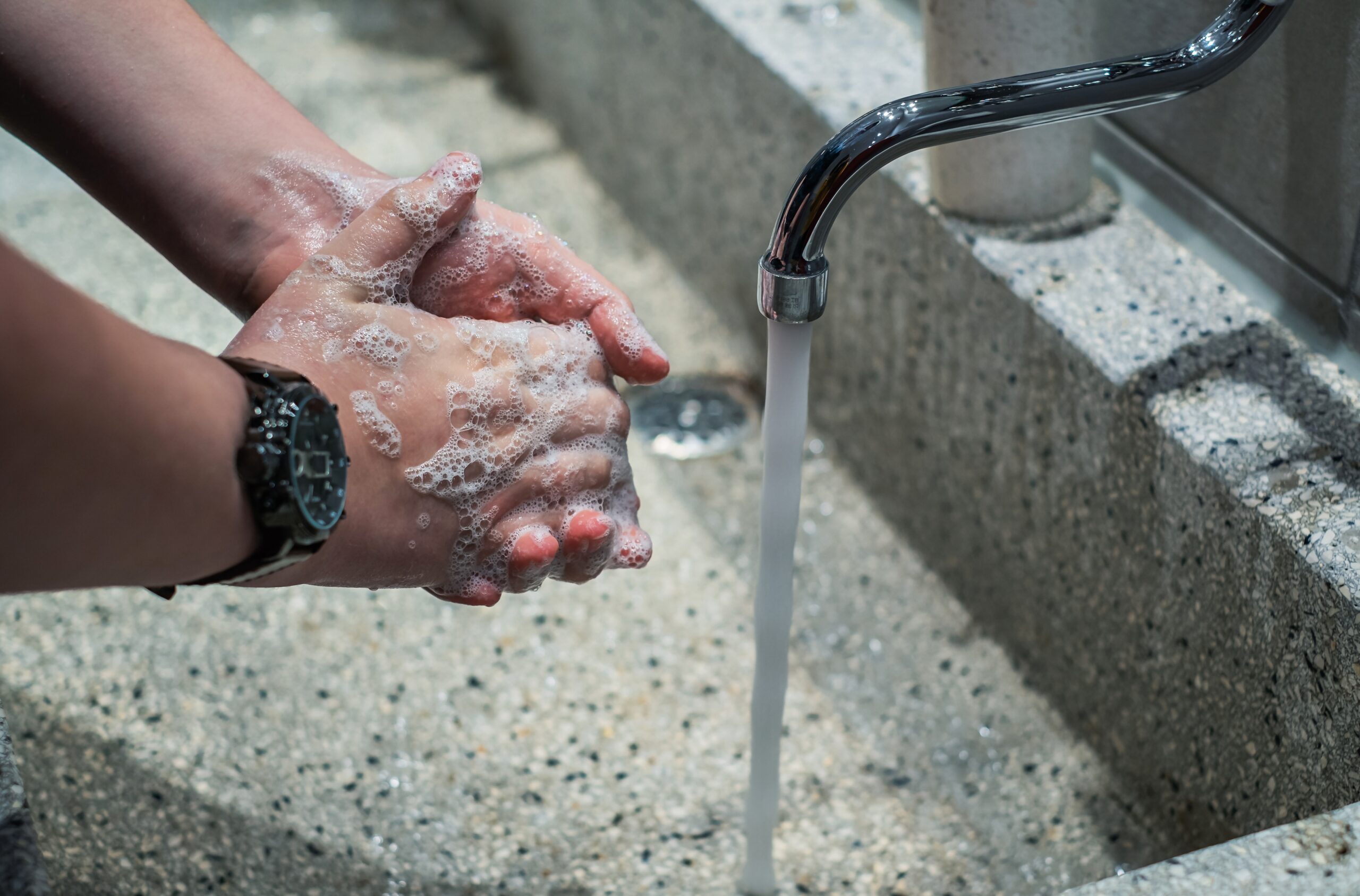 Close-up of hands being washed with soap under running water from an outdoor tap