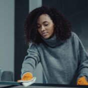 A woman in a gray sweater wipes a table with care, showcasing home cleaning in comfort.