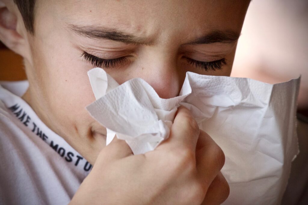 Boy blowing his nose into a tissue.