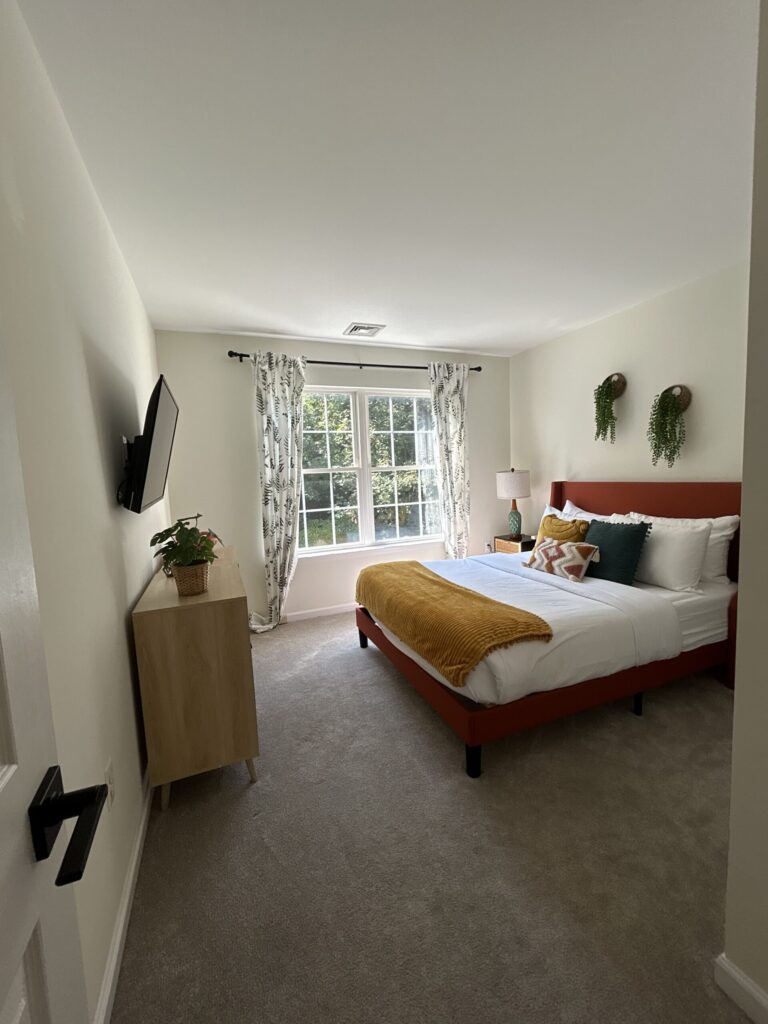 Neatly made bed with white bedding and a mustard throw in a bright bedroom.
