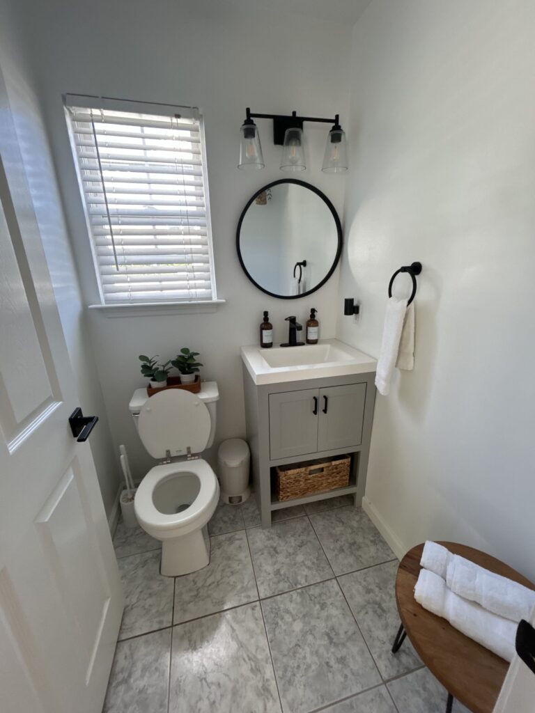 Bathroom with a white vanity, round mirror, toilet, and folded towels.