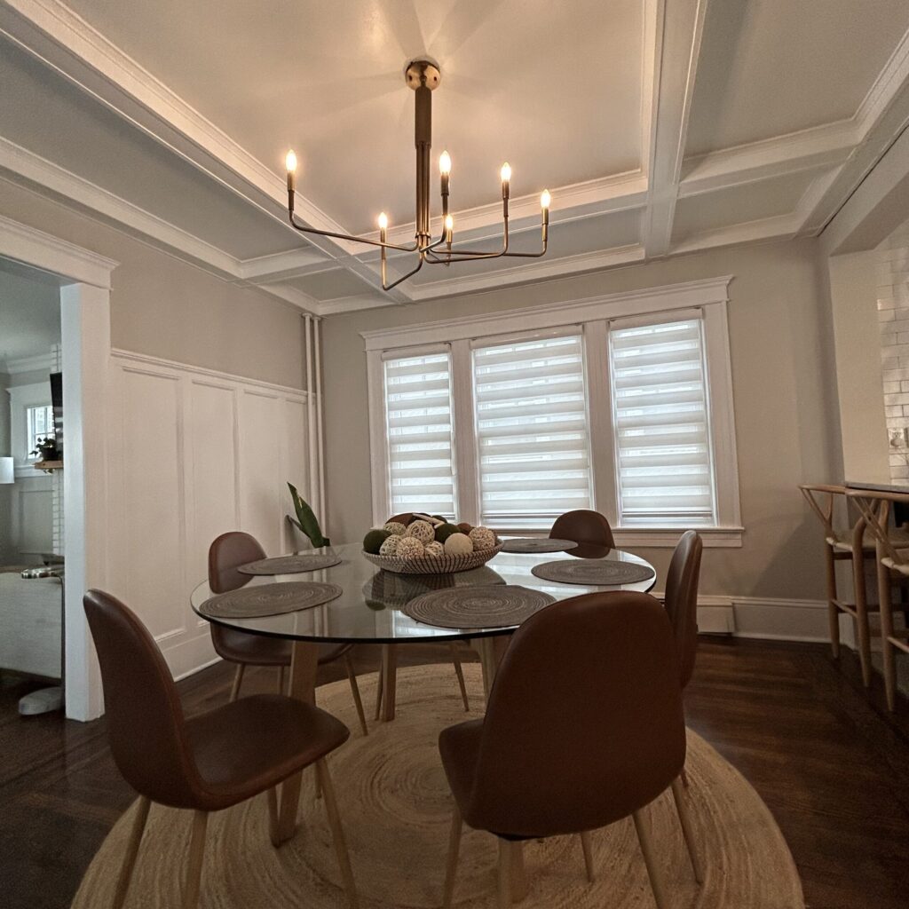 Dining room with coffered ceiling, brass chandelier, and round glass table.