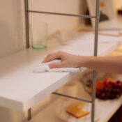 A hand wiping dust off a white shelf with a cloth to reduce allergens in your home