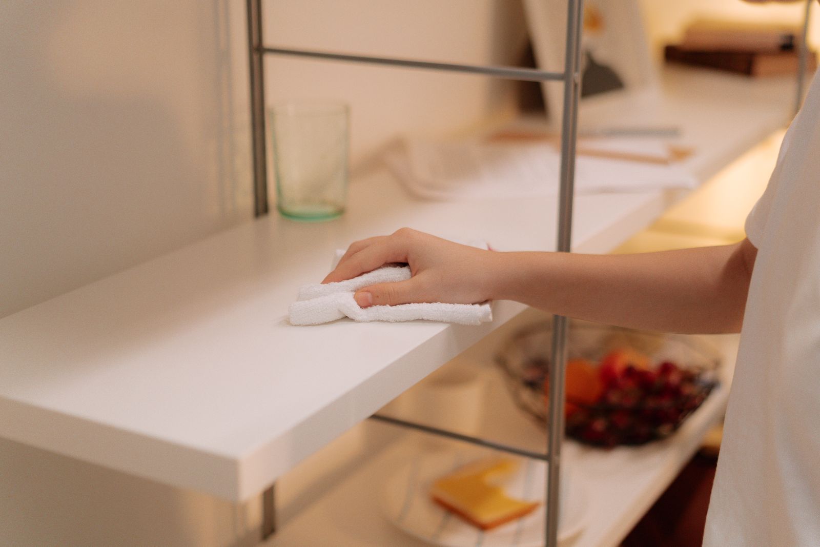 A hand wiping dust off a white shelf with a cloth to reduce allergens in your home