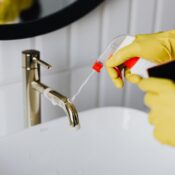 Gloved hands spraying and wiping a bathroom faucet during a deep cleaning